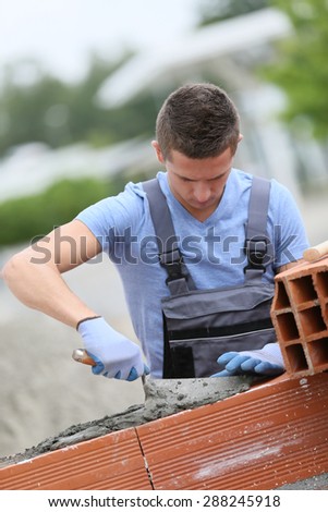 Young brick layer working outside on brick wall construction