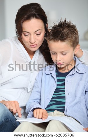 Little boy and mother sitting on sofa at home with book