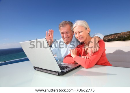 Senior couple waving at web-camera on laptop computer
