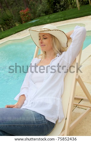 Blond woman resting in long chair by swimming-pool