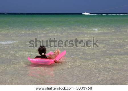 Young girl on pink air-bed in the Mediterranean Sea. Monastir, Tunisia.