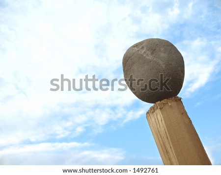 A round stone in balance on a pole against the sky