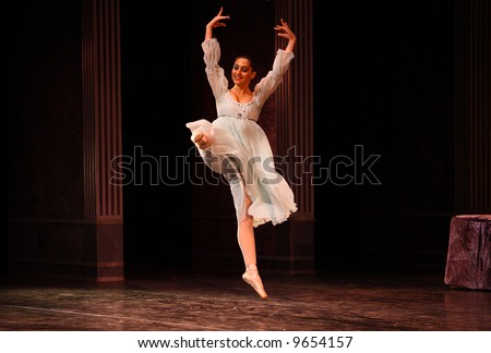 female classic ballet dancer dressed white making the jump it by stage lights