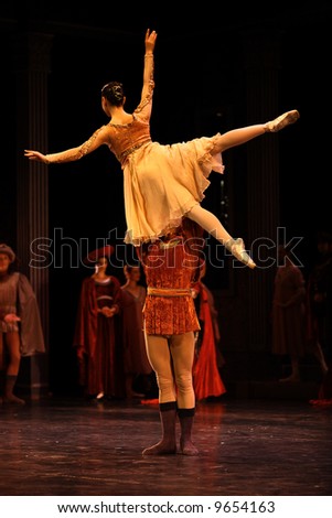 male classic ballet dancer dressed brown holds female ballet dancer dressed white