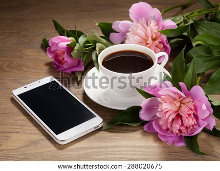 Smartphone, a cup of coffee and flowers on old table.