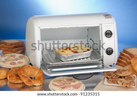 Electric oven-toaster on a reflective surface with diversity of baked and toasted food