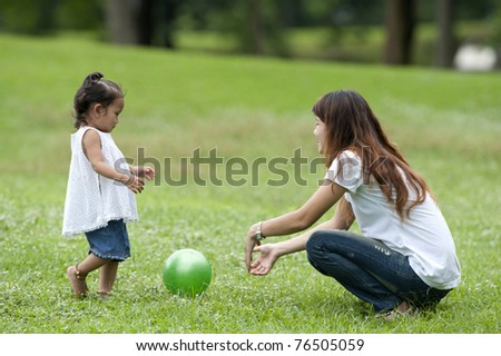 Mother teaching daughter to soccer/ball in the park happily.