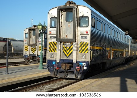 Two passenger rail cars side-by-side on parallel tracks in station