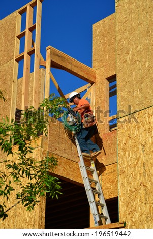 BAKERSFIELD, CA-JUNE 2, 2014: Three story low rent senior apartments are on schedule for end-of-year completion. An unidentified workman carries power tools and extension cord up a ladder.