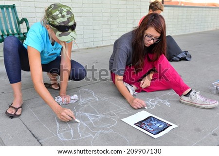 TEHACHAPI, CA - AUGUST 9, 2014: Two unidentified high school girls share sidewalk art work duties for their entry in the annual Chalk on the Walk competition.