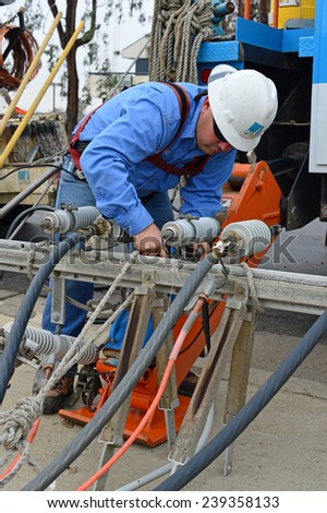 BAKERSFIELD, CA - DECEMBER 21, 2014: The local utility company is replacing a wood pole. An electrician rigs a steel crossarm for hoisting into place on the new pole.
