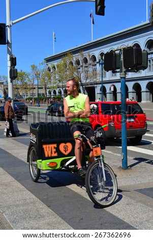 SAN FRANCISCO, CA - MARCH 29, 2015: An owner of a bicycle taxi service pauses on his human-powered vehicle to look for customers among the tourists in front of the Ferry Building.