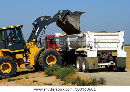 KERN COUNTY, CA - AUG 20, 2015: A front end loader discharges excess dirt from a construction project into a bottom dump truck which will take the material off site.