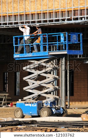 Workmen install metal studs from scissor lift platform