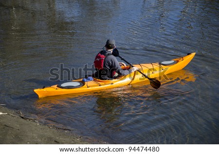 A river explorer launches his kayak from the shore