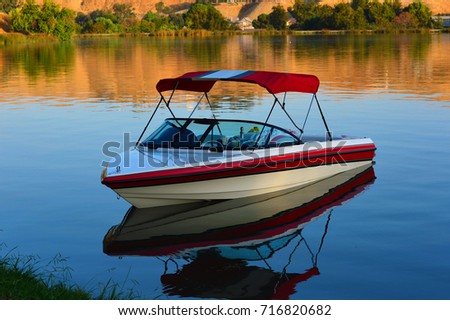 A small outboard runabout boat with canopy lies at anchor on a placid lake. Stock fotó © 