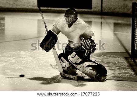 Goalie in generic white jersey with generic red goalie mask makes a tremendous diving attempt to prevent the puck (frozen in flight) from entering the goal