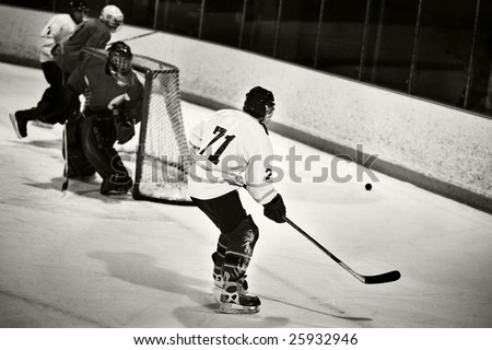 Focus on ice hockey player as he prepares to play the puck.  Goalie and two other players out of focus in background.