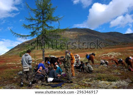 SAYAN MOUNTAINS, RUSSIA - AUGUST 22: Group of tourists resting on the mountain pass under a lone larch on august 22, 2012 in Sayan Mountains, Russia. Larch marks the border between Buryatia and Tuva.