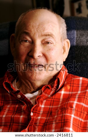 A handsome man in his seventies, wearing a red flannel shirt, smilling.
