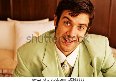 A businessman in a green suit relaxing on a hotel bed and smiling