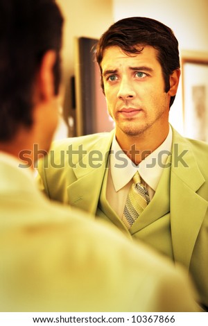 Business man in a green suit taking stock of himself in the mirror.