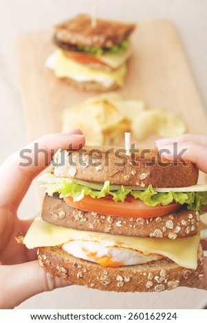 Person holds egg sandwich and another one in the background on wooden board