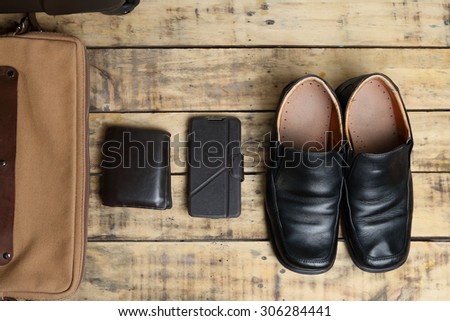 Black leather shoes, wallet, mobile smart phone and  luggage travel bag on the wooden table