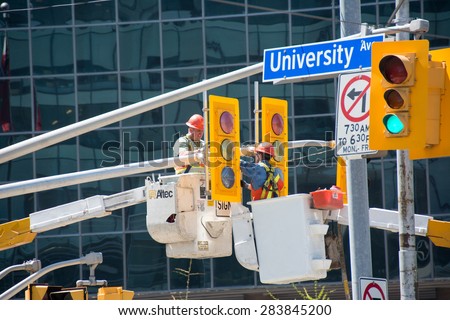 TORONTO,CANADA-MAY 25,2015: Guild of Electric workers: Construction workers in buckets working on University Ave traffic light in front of commercial building.