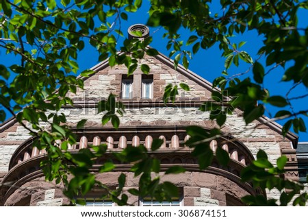 Close-up of the top triangular structure of Victoria university building seen through branches. Victoria University is a college of the University of Toronto, founded in 1836