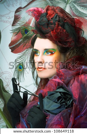 Portrait of young lady in hat with peacock feathers and in blue beads on her hand.