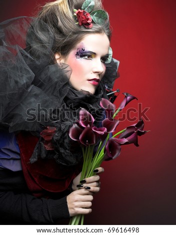 Romantic portrait of young woman in creative image abd with dark flowers in her hands