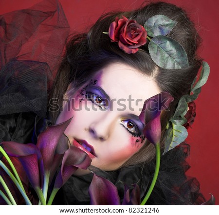 Romantic portrait oj young woman in creative image and with dark flowers in her hands