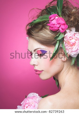 Portrait of young charming woman with  flowers in her hair on the pink background