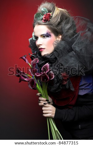 Romantic portrait of young woman in creative image and with dark flowers in her hands