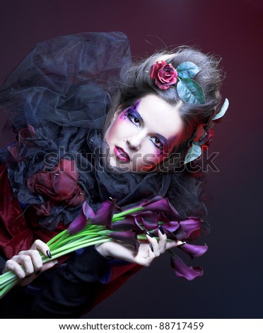 Romantic portrait of young woman in creative image and with dark flowers in her hands