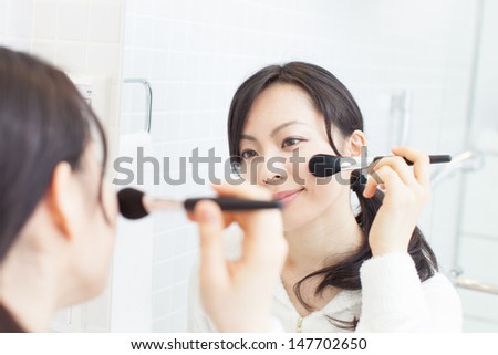 beautiful young woman applies makeup in front of a bathroom mirror