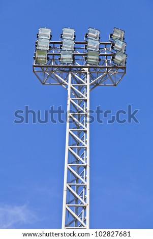 The high tower of a large stadium lighting structure against a blue sky.