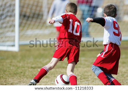 two soccer boys fighting for the ball with goalie in the background