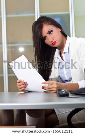 Beautiful woman sitting behind the desk and reading files in the office