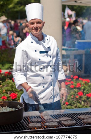 smiling chef cooking burgers outdoors on a nice summer day