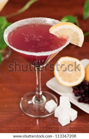 Huckleberry lemon drop martini close up on a bar top with fresh ingredients on the side, garnished with a sugar rim and a lemon slice