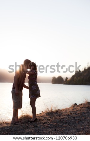 young couple kissing on the shore with the sun behind them, dramatic and low color
