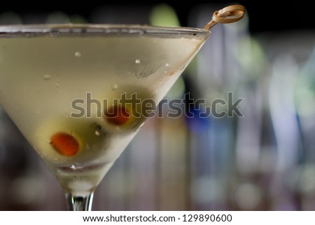 dirty martini chilled and served on a busy bar top with a shallow depth of field and color lights and glasses in the background