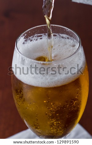 golden beer poured in to a chalice on a busy bar top with a shallow depth of field showing lights and glassware out of focus in the background