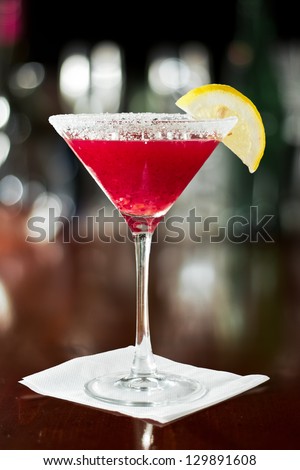 closeup of a lemon drop martini on a busy bar with glassware in the background