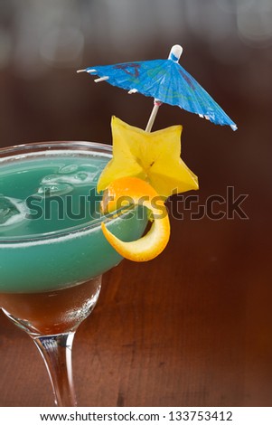blue hawaiian cocktail served on a busy bar top garnished with a carambola slice and an umbrella