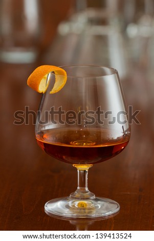 brandy snifter filled with an orange liquor served on a busy bar top garnished with an orange twist