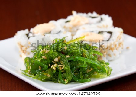 seaweed salad closeup with sushi rolls in the background served on a white plate