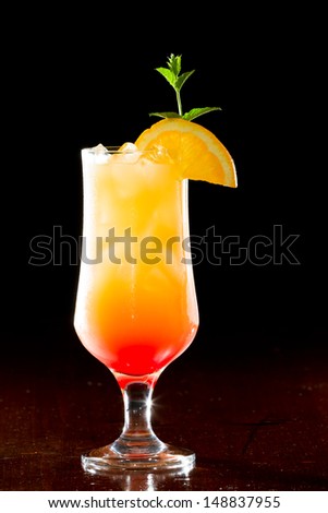 tequila sunrise, fresh orange juice with tequila and cherry juice served in a stem glass on a dark bar